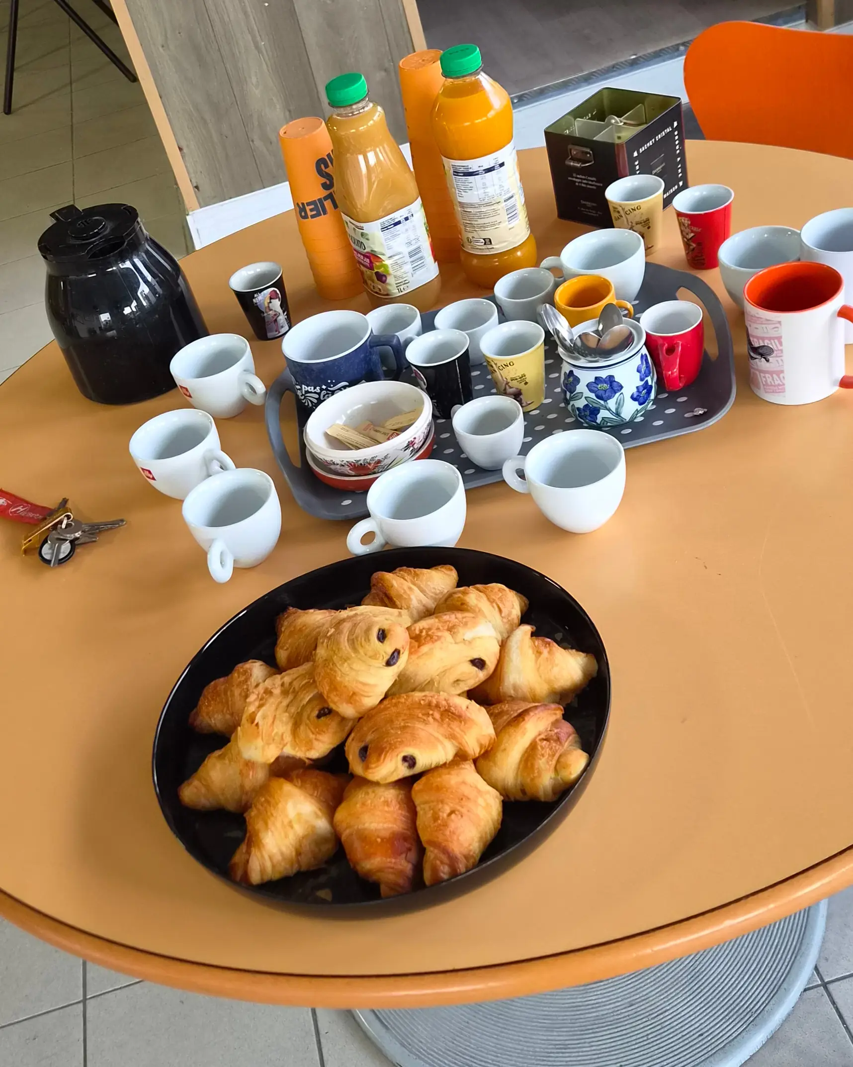 Café, jus d'orange et viennoiseries servis sur la table ronde de l'accueil de l'atelier.