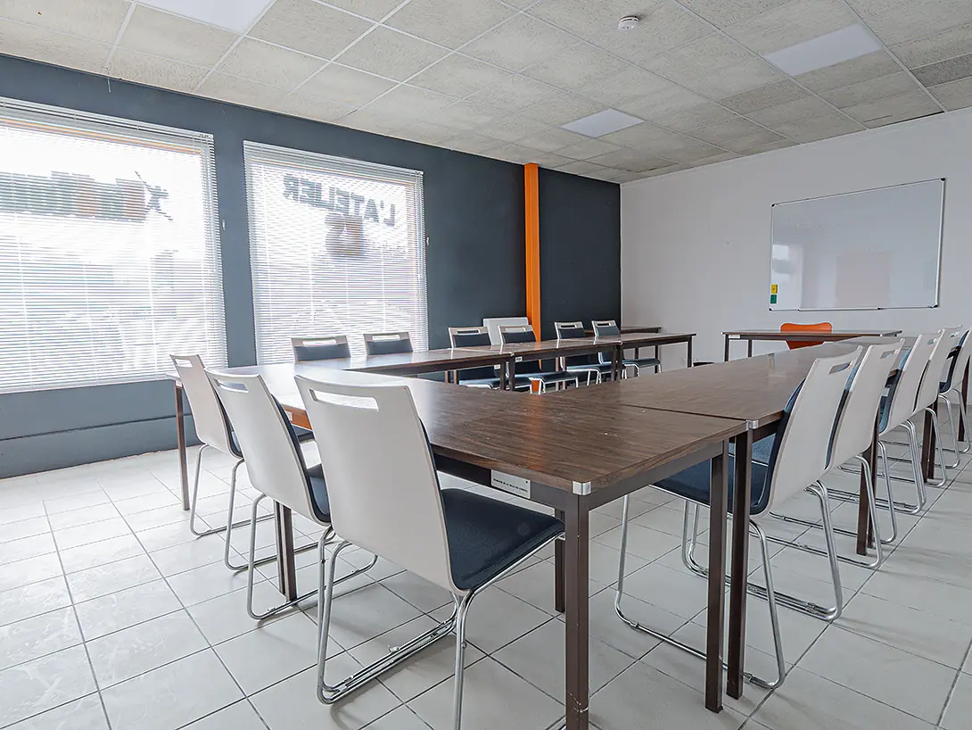 La salle de réunion de L'Atelier KS : tables, chaises blanches, tableau blanc et deux baies vitrées.