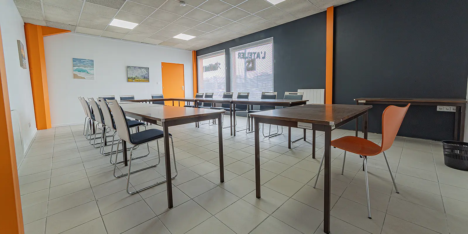 La salle de réunion vide, à La Rochelle, chez L'Atelier KS : tables et chaises blanches, tableau blanc au fond, baies vitrées avec stores.