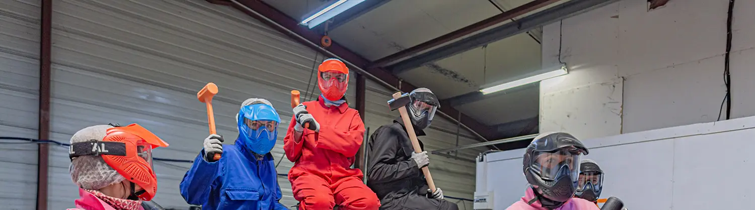 Une équipe en combinaison, masque et gants, masses et battes en main, assise sur une voiture avant sa séance de team building à La Rochelle, à L'Atelier KS.