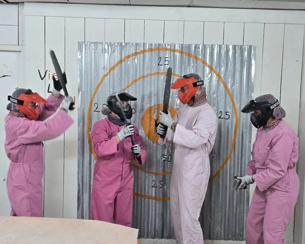 Quatre participants en combinaison, masque et gants, battes en main devant la cible de tôle de la salle.